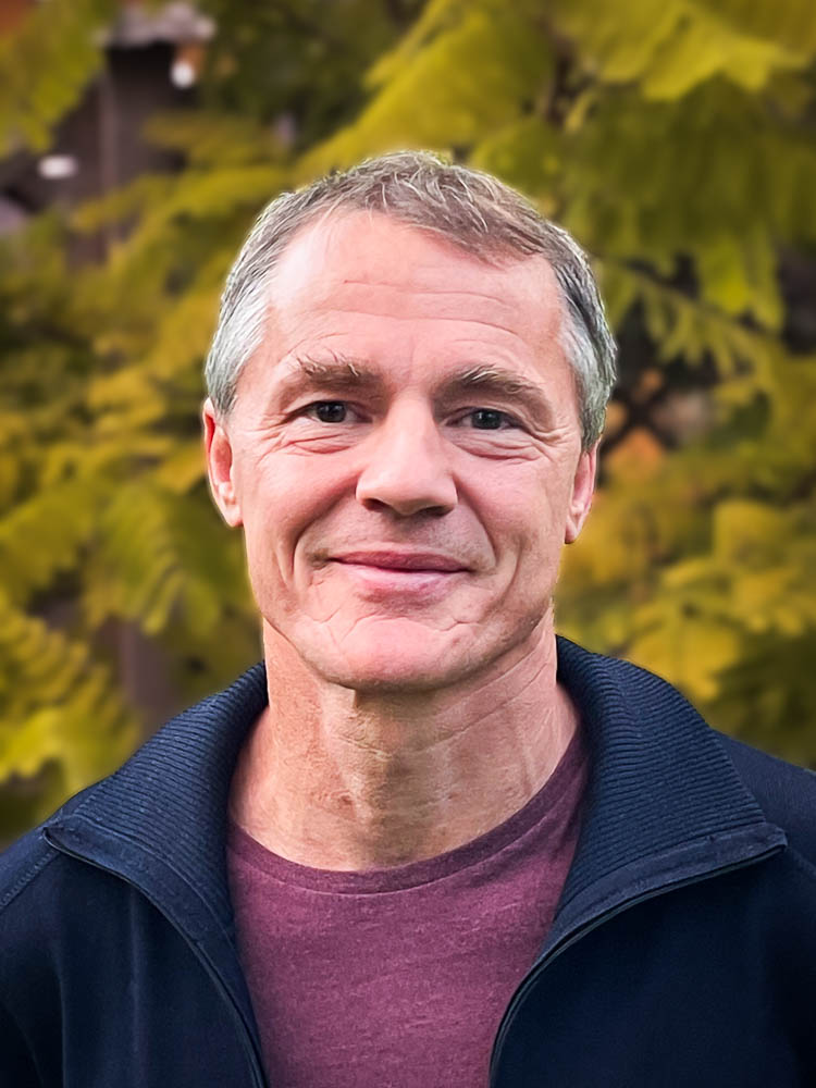 Johannes Michels schaut freundlich in die Kamera vor einem herbstlichen Bokeh im Hintergrund.